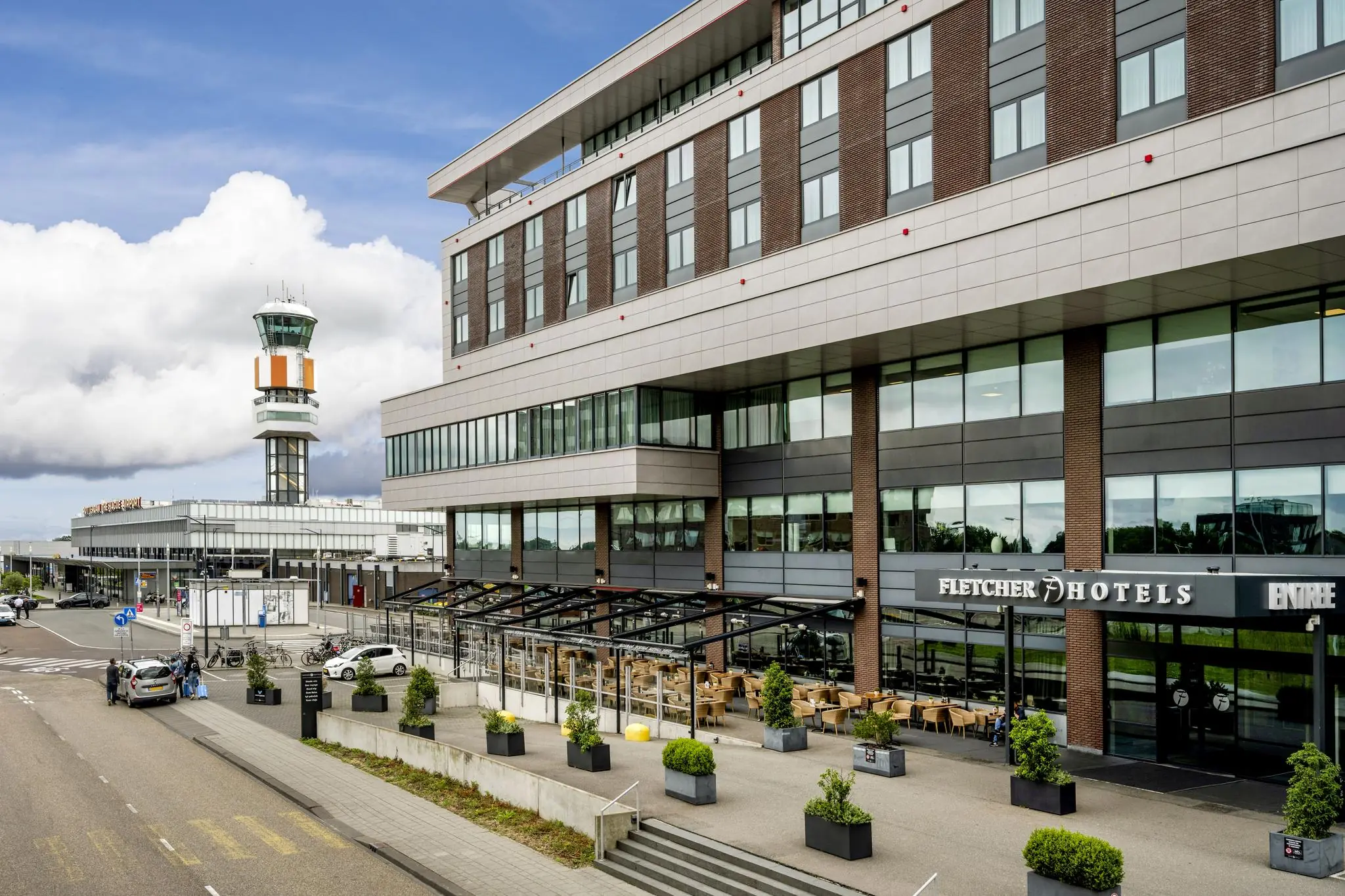 Vooraanzicht van Fletcher Hotel bij Rotterdam The Hague Airport met terras en verkeerstoren op de achtergrond.